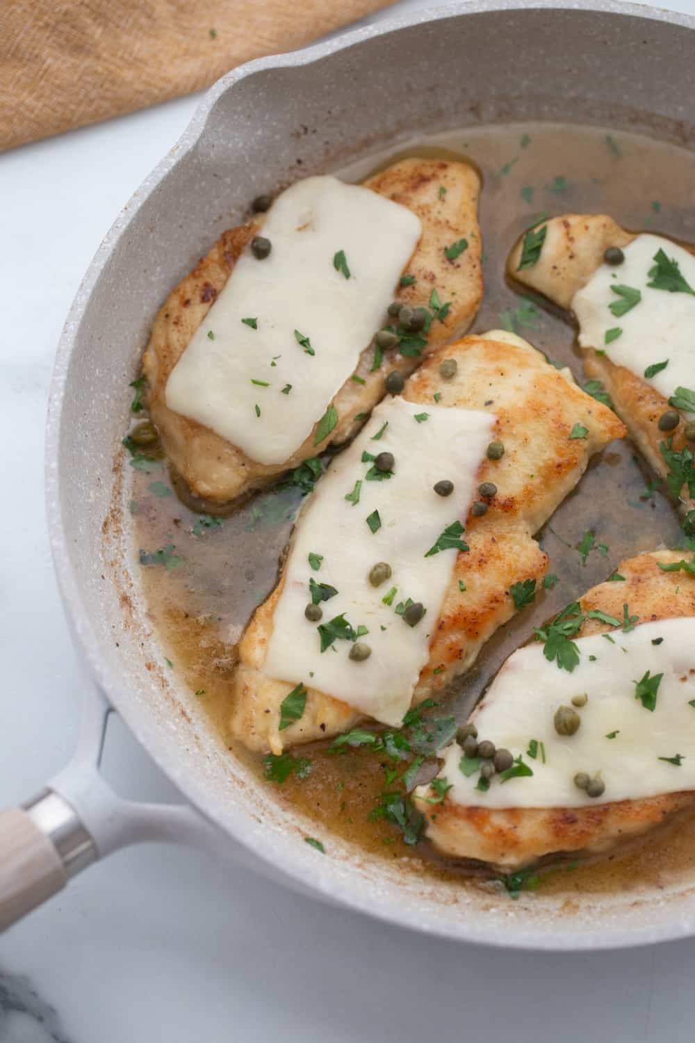 Chicken scallopini in a white ceramic pan topped with thin mozzarella, capers, and fresh parsley.