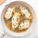 Chicken scallopini in a white ceramic pan topped with thin mozzarella, capers, and fresh parsley.