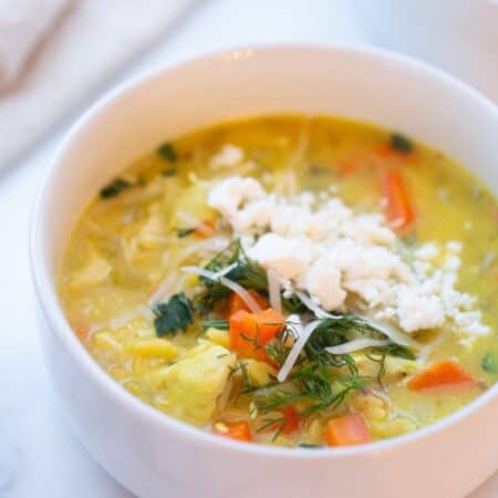 Bowl of lemon chicken orzo soup topped with fresh dill, shredded parmesan, and crumbed feta.