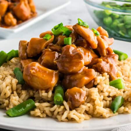 Easy homemade bourbon chicken plated over brown rice with green beans and garnished with green onions.
