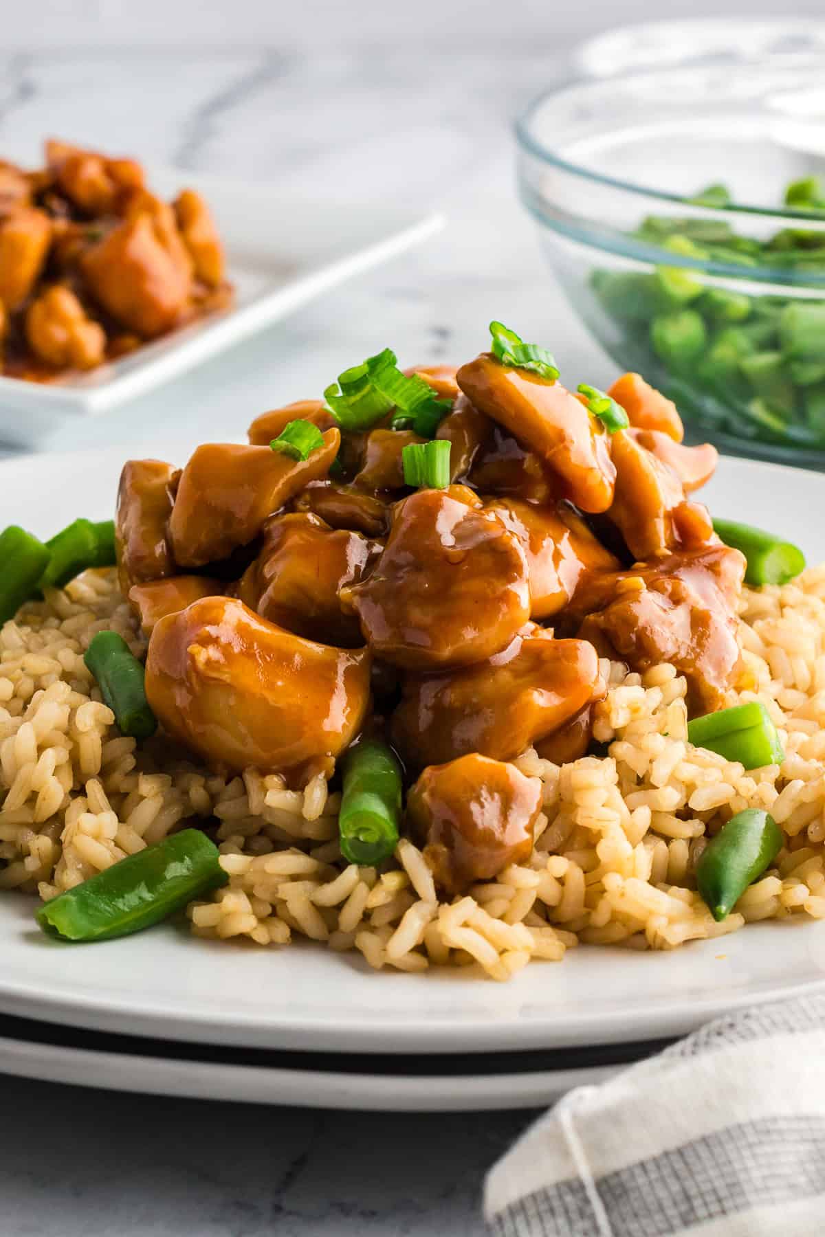 Easy homemade bourbon chicken plated over brown rice with green beans and garnished with green onions.