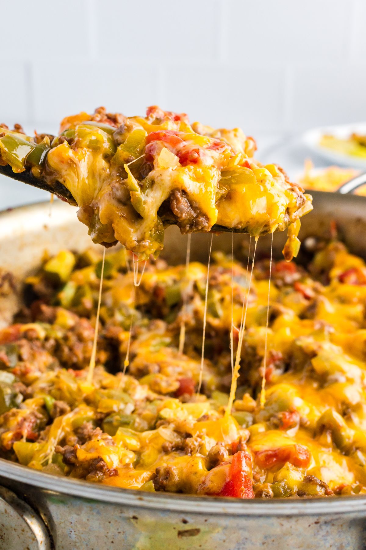 Close-up of a wooden spoon lifting a portion of gooey taco zucchini skillet with melted cheese and chunks of vegetables and meat.