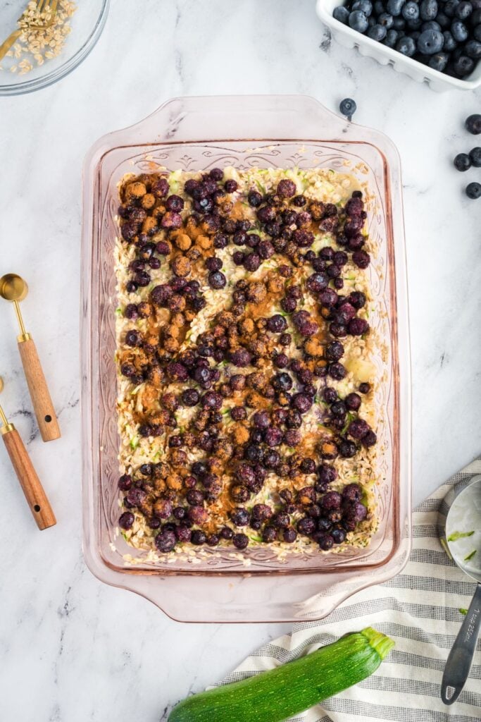 A glass baking dish filled with oatmeal mixture, topped with fresh blueberries and a sprinkle of cinnamon, ready to be baked.