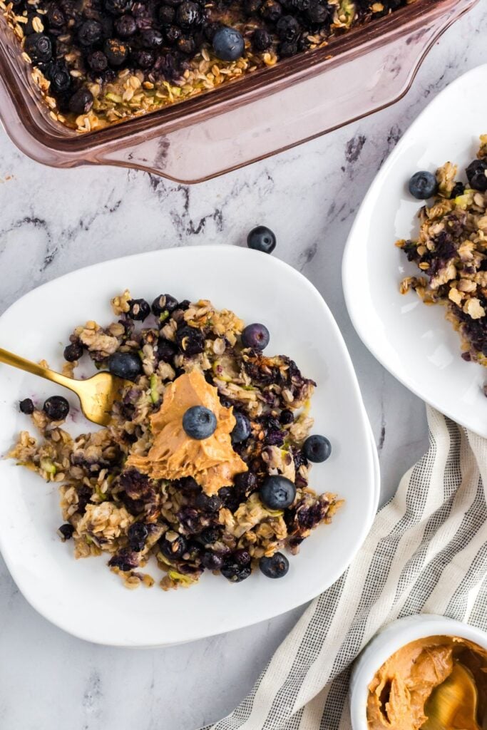 A serving of zucchini blueberry baked oatmeal on a white plate, topped with peanut butter.