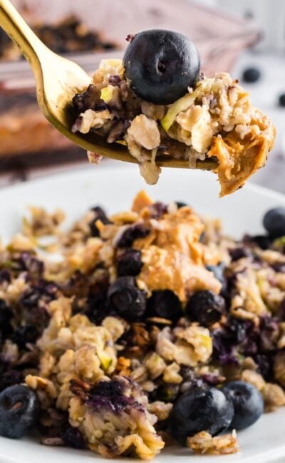 A serving of zucchini blueberry baked oatmeal on a white plate, garnished with fresh blueberries and a gold fork.