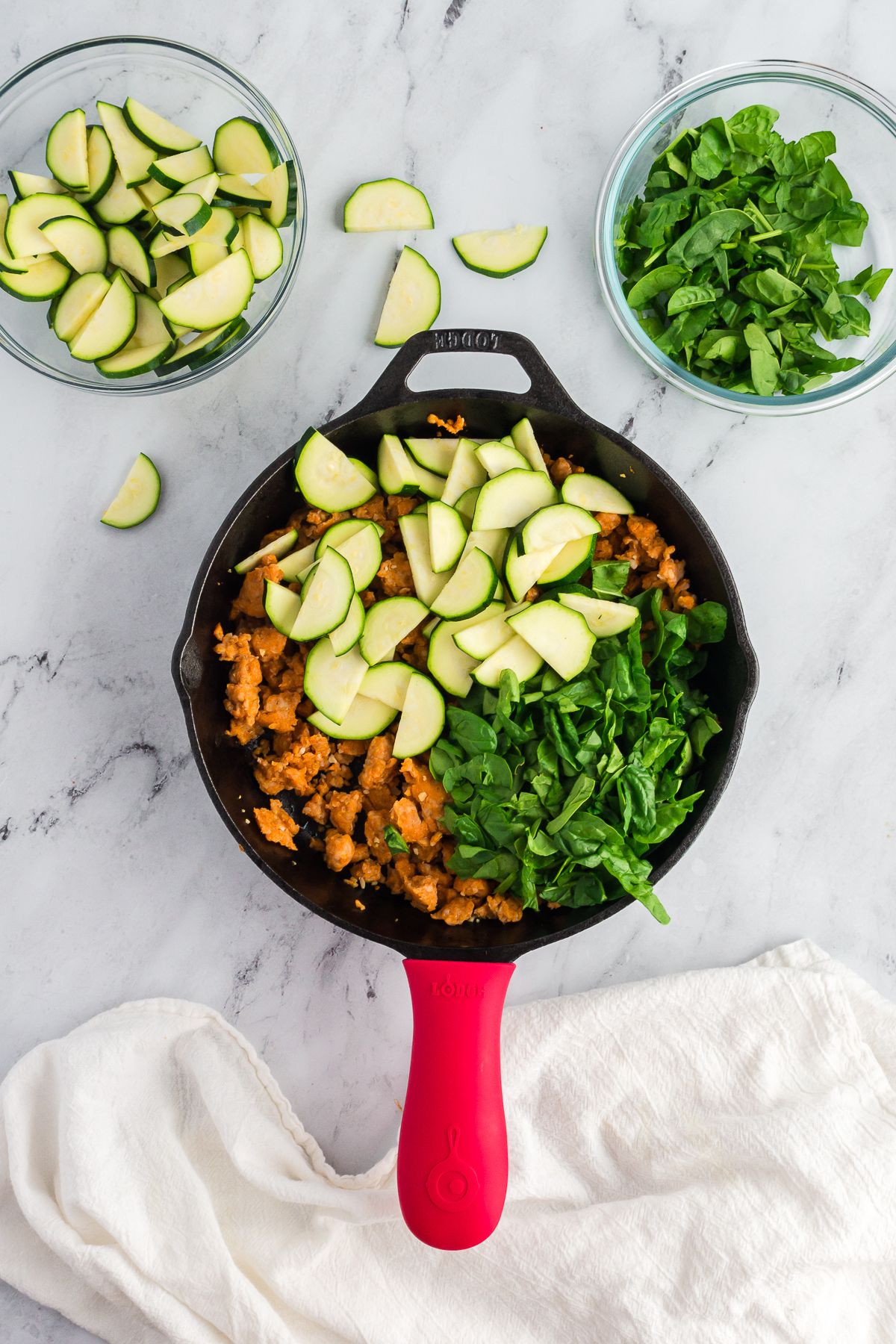 A skillet with ground chicken sausage, zucchini, and spinach.