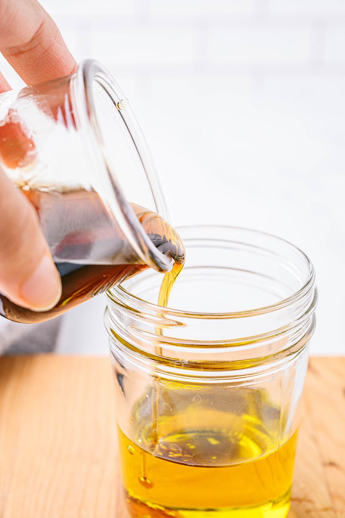 Close-up of maple syrup or honey being poured into a glass jar with avocado or olive oil for apple cider vinaigrette.