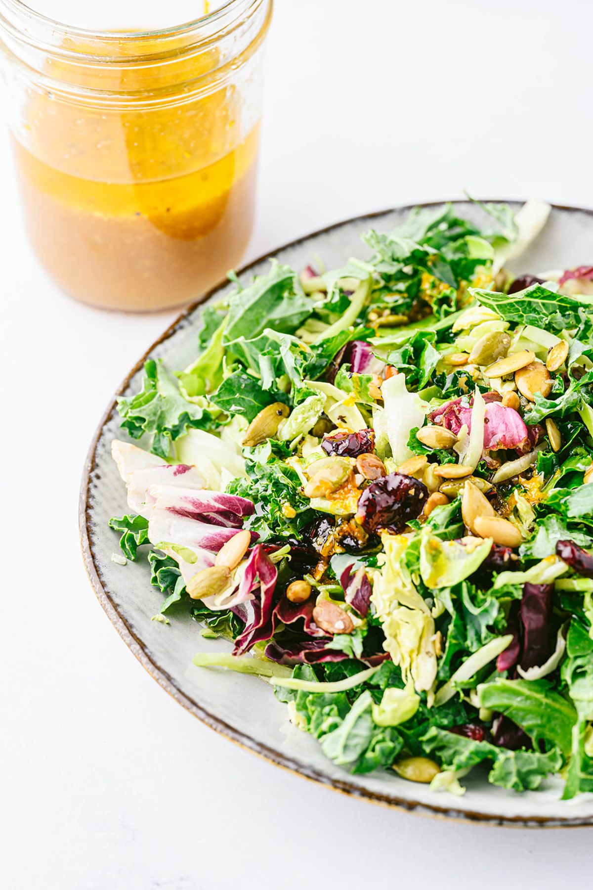 A jar of freshly mixed apple cider vinaigrette next to a holiday salad.