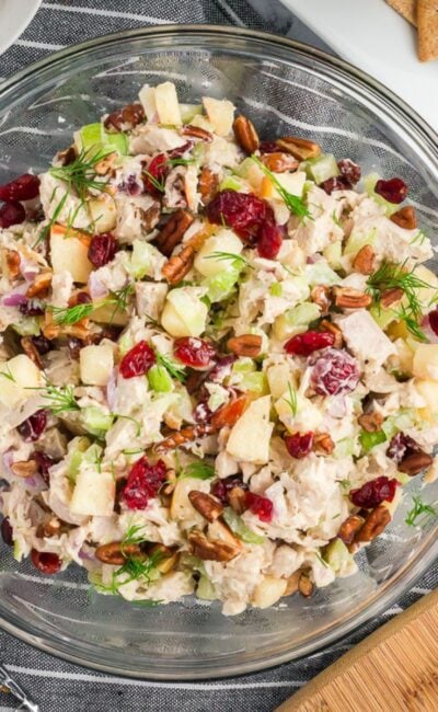 The fully mixed turkey salad in a clear bowl, showing chunks of turkey, diced apple, cranberries, and pecans coated in a creamy dressing on a white marble tabletop.