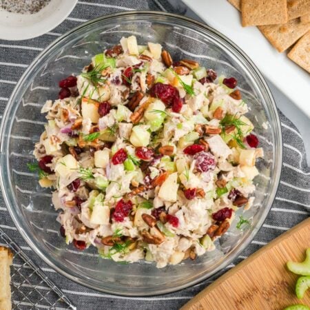 The fully mixed turkey salad in a clear bowl, showing chunks of turkey, diced apple, cranberries, and pecans coated in a creamy dressing on a white marble tabletop.