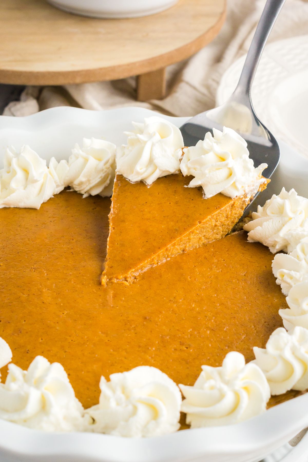 A close-up of a slice of crustless pumpkin pie on a white plate, topped with whipped cream, with a gold fork standing upright in the center.