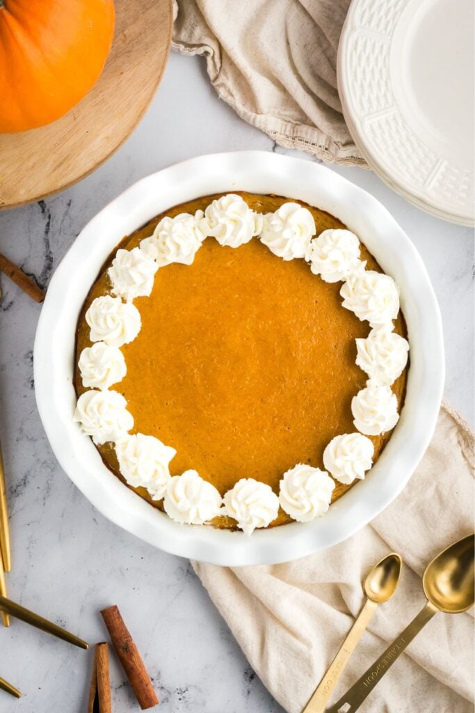 A crustless pumpkin pie in a white pie dish, decorated with whipped cream swirls around the edge.