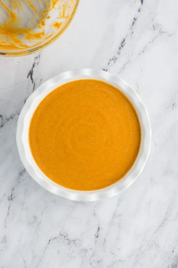 Pumpkin pie filling in a glass pie plate ready to cook.