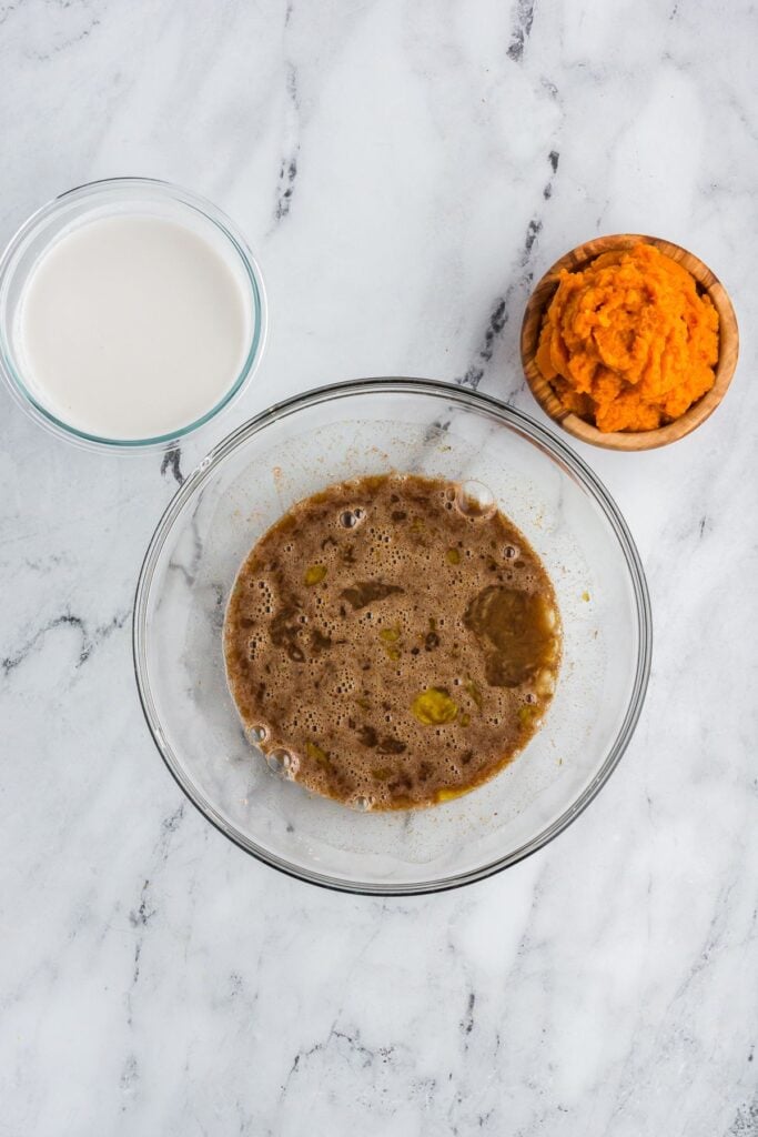 Coconut milk, pumpkin puree, and egg and maple syrup mixture in glass bowls for pumpkin pie.