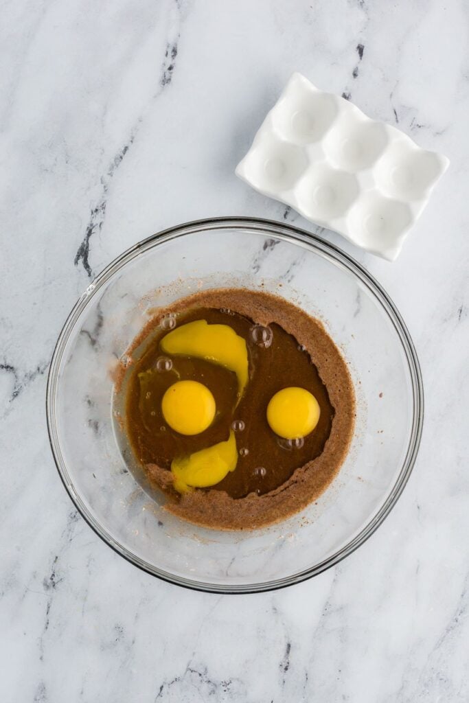 Three eggs in a glass bowl with maple syrup and spices.