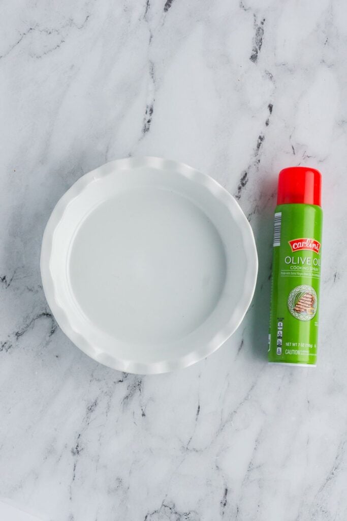 A pie plate with nonstick cooking spray sitting next to it on a marble counter.