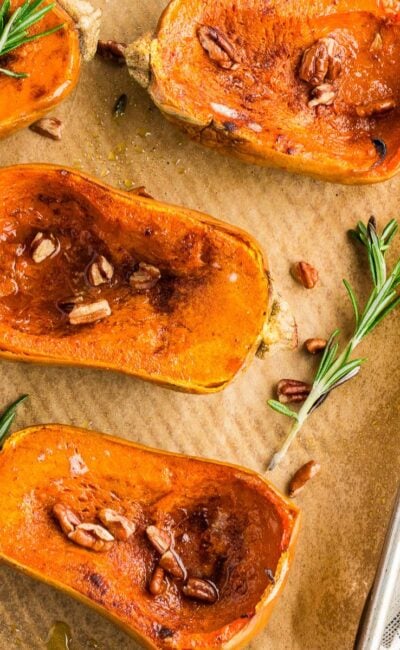 Roasted honeynut squash on a sheet pan garnished with fresh rosemary, pecans, and cinnamon.