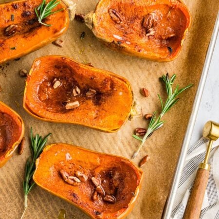 Roasted honeynut squash on a sheet pan garnished with fresh rosemary, pecans, and cinnamon.