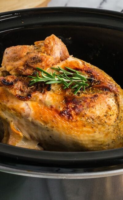 Perfectly cooked turkey breast with a golden crust and rosemary garnish in a slow cooker, ready to serve.