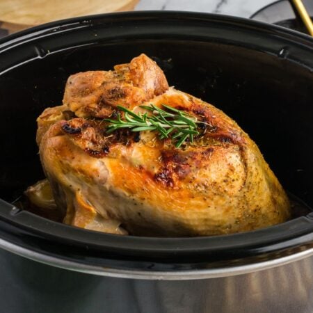 Perfectly cooked turkey breast with a golden crust and rosemary garnish in a slow cooker, ready to serve.