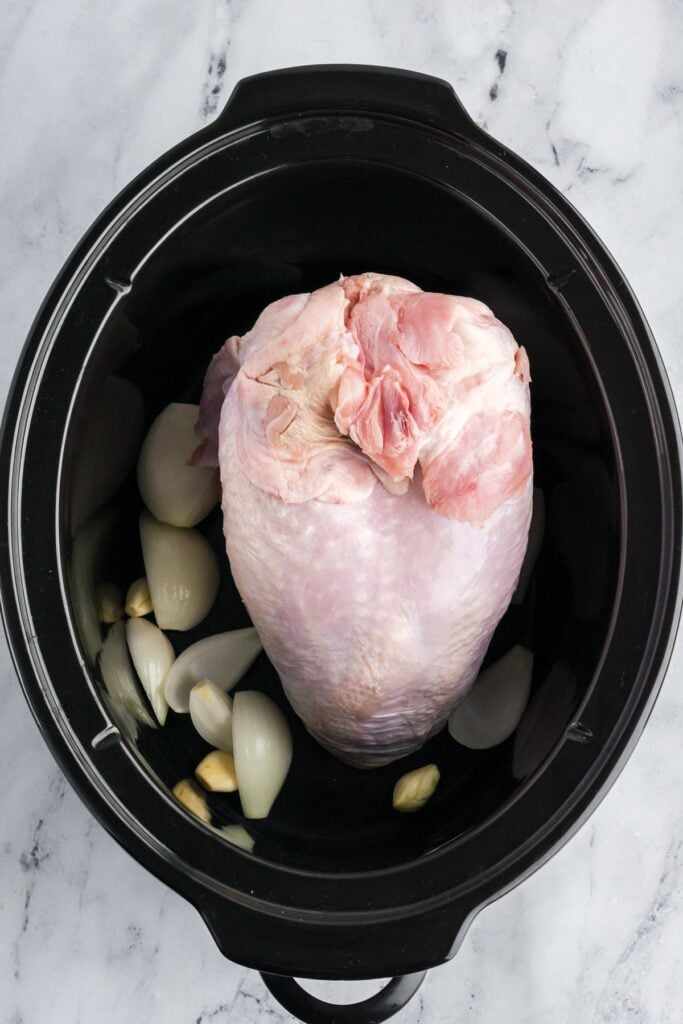 Raw turkey breast in a crock pot over onions and garlic.