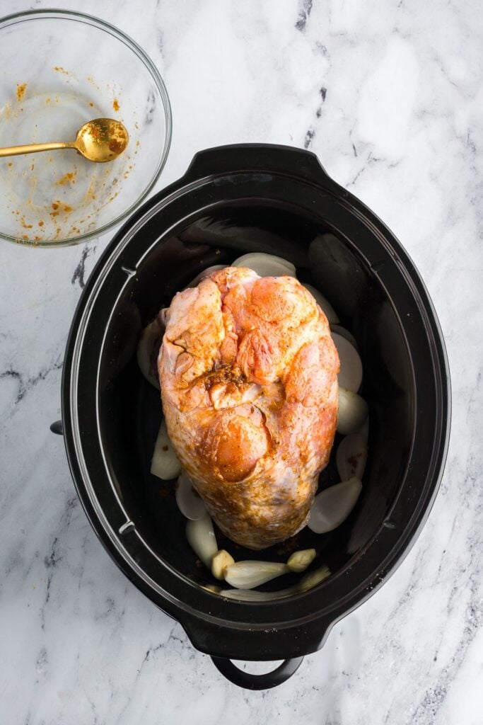 Seasoned raw turkey breast placed on a bed of onions and garlic in a slow cooker, prepped for cooking.