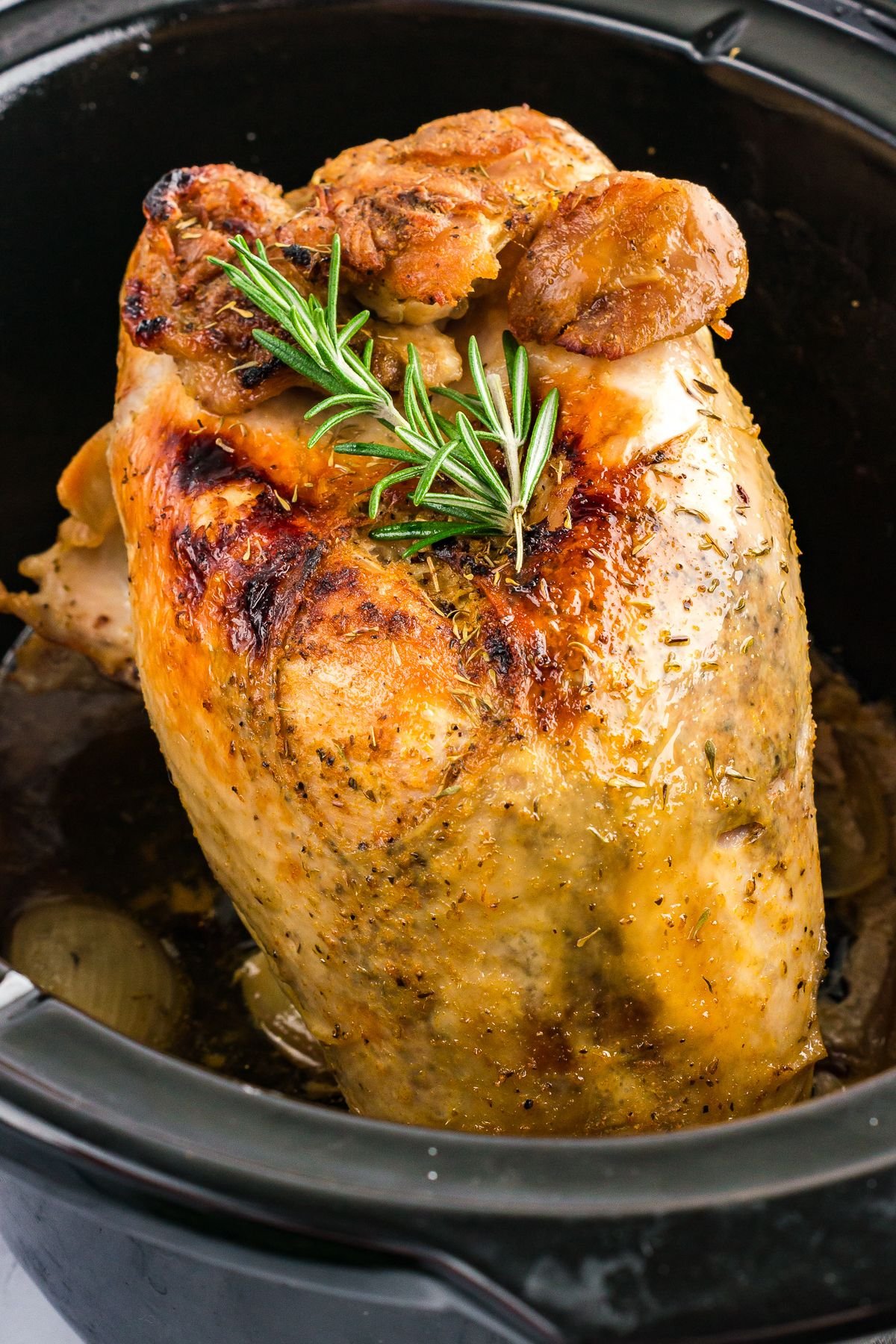 Golden-brown slow-cooked turkey breast with crispy skin, garnished with fresh rosemary, resting in a crock pot.