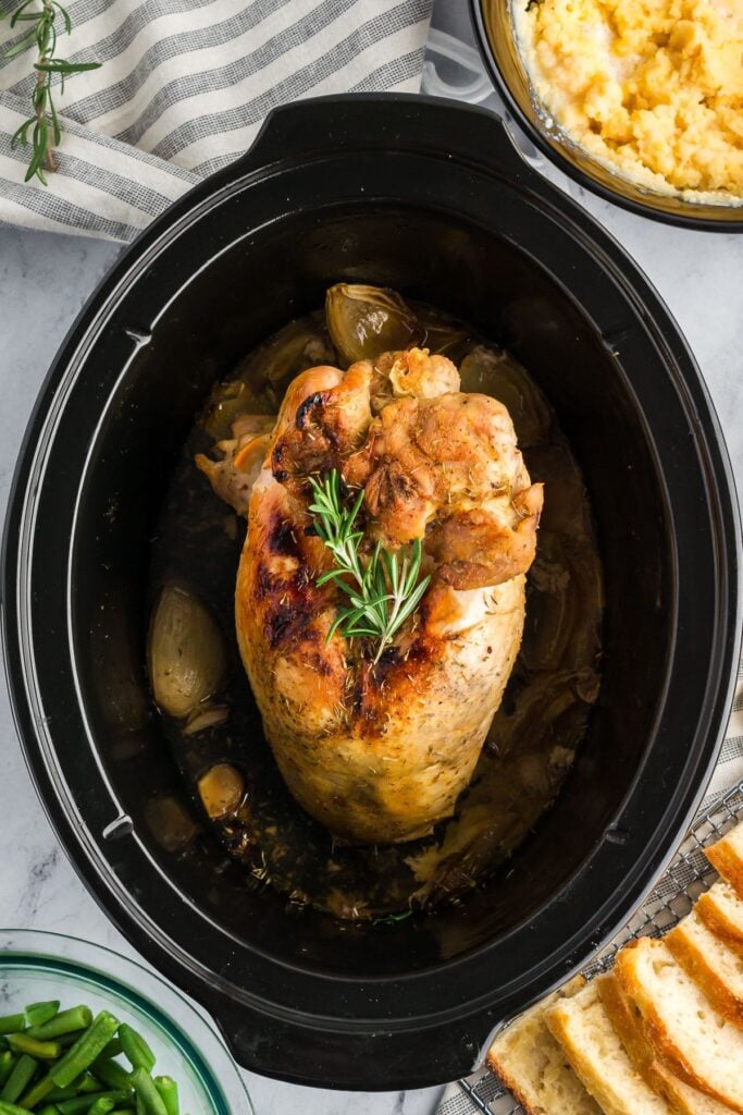 Perfectly cooked turkey breast with a golden crust and rosemary garnish in a slow cooker, ready to serve.