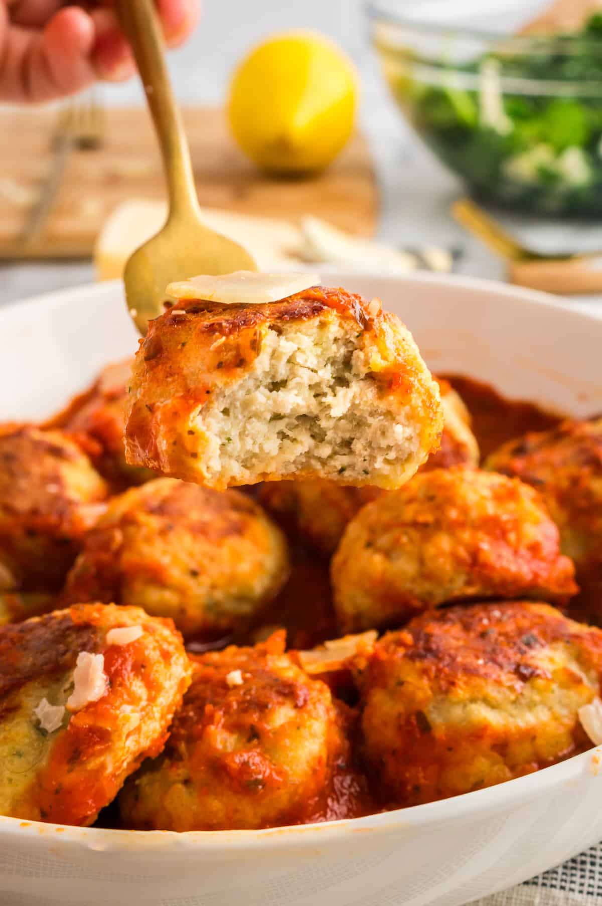 A fork holding a bitten into chicken meatballs.