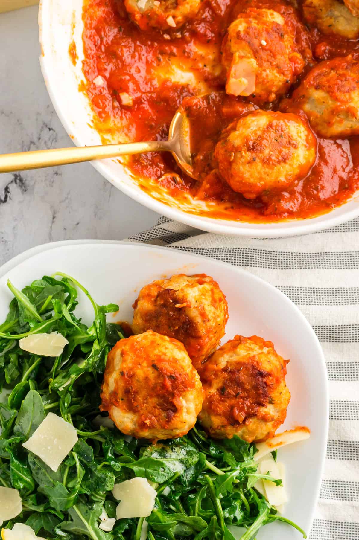 A serving bowl of chicken meatballs next to a plate of salad and meatballs.