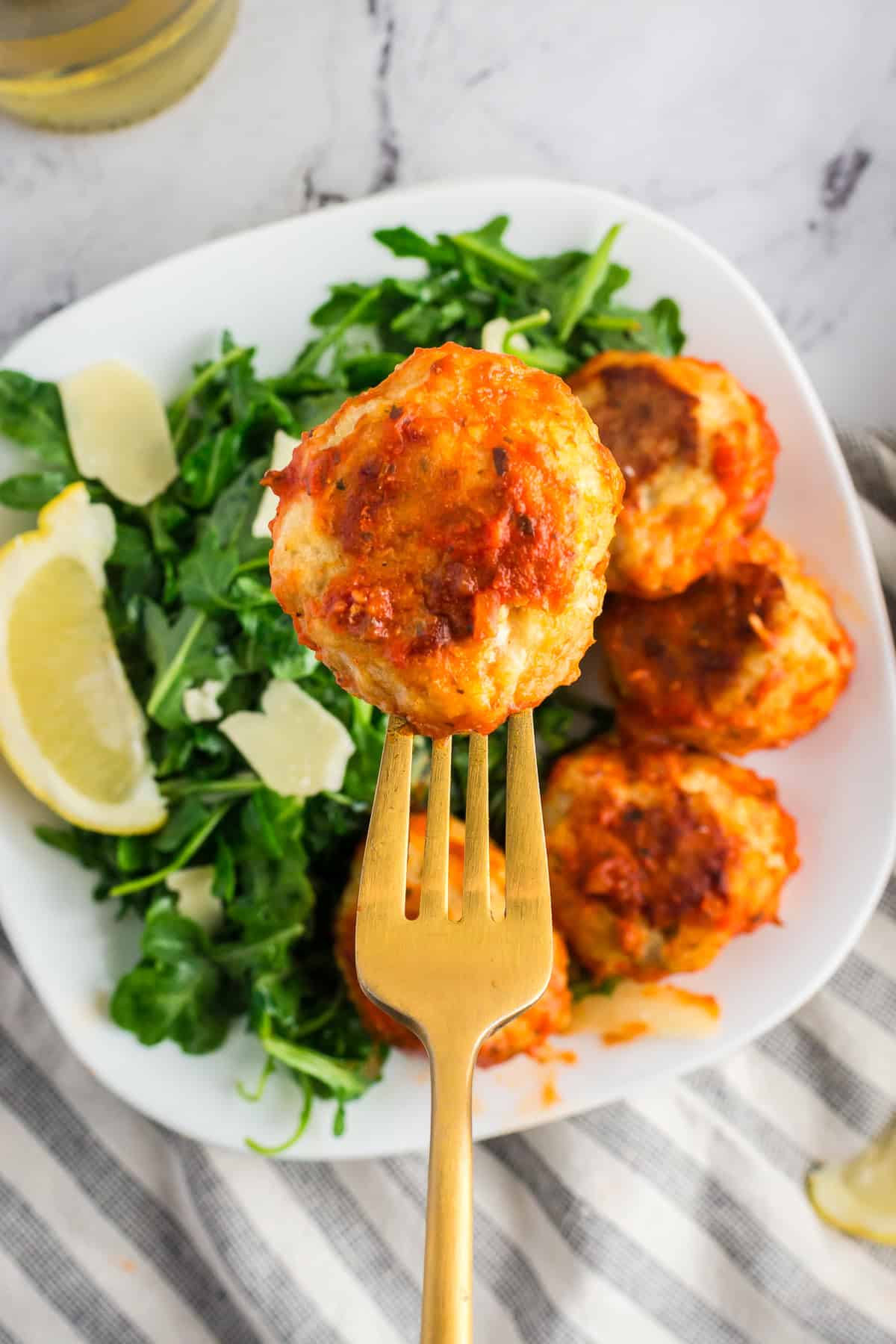 A fork holiday a baked chicken meatball covered in sauce over a bowl of arugula.