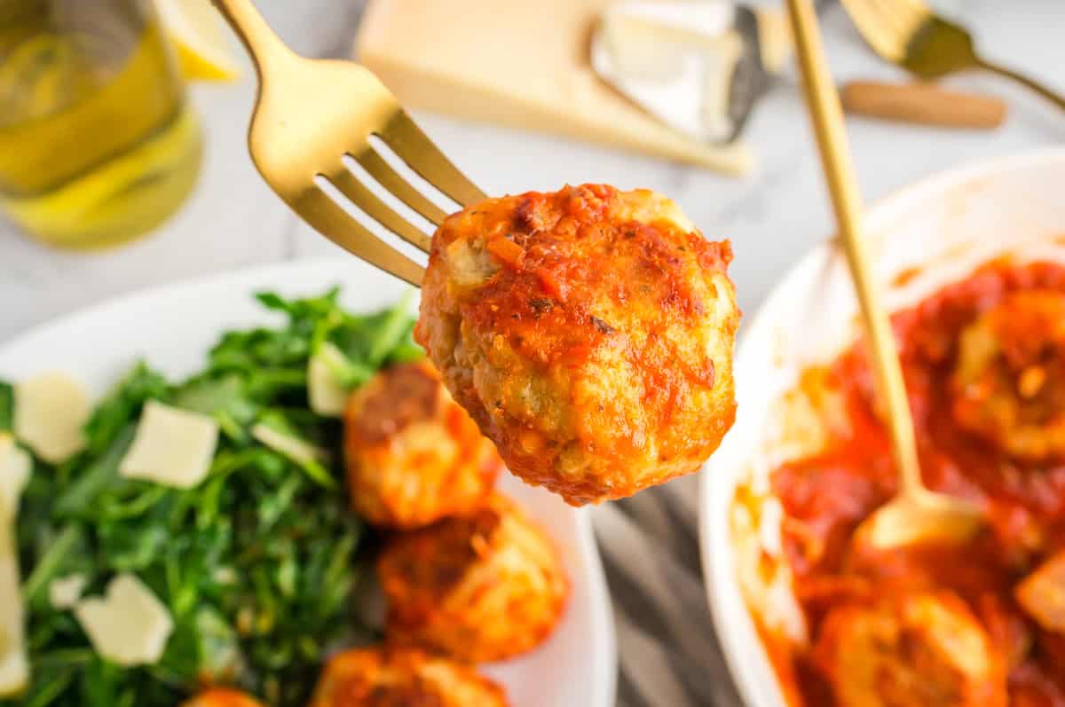 A fork holding a chicken meatball covered in sauce.