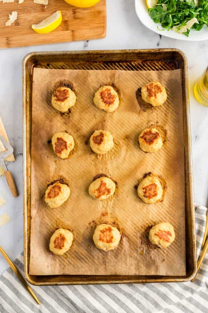 Browned baked chicken meatballs on a sheet pan covered with parchment paper.