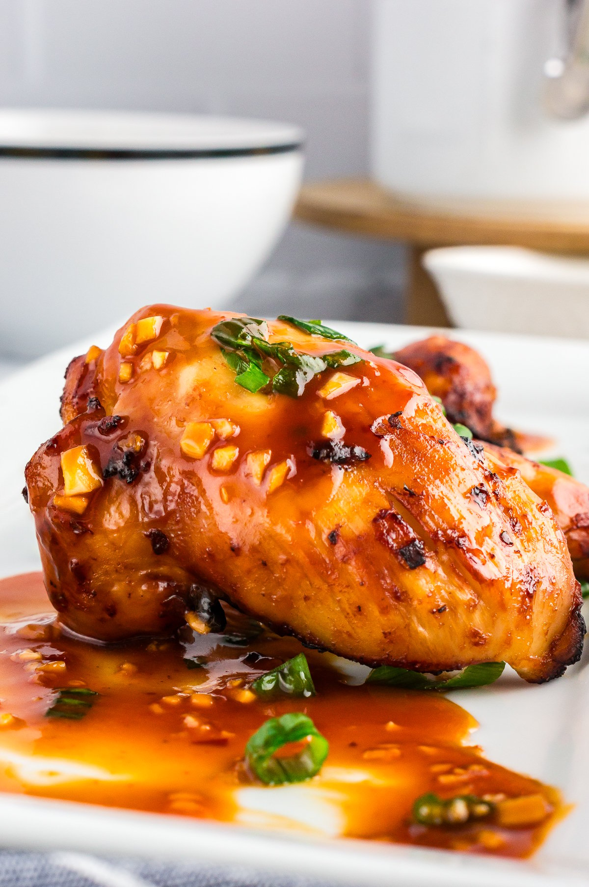 Close up shot of sticky air fryer chicken thighs on a white plate shot from the side.