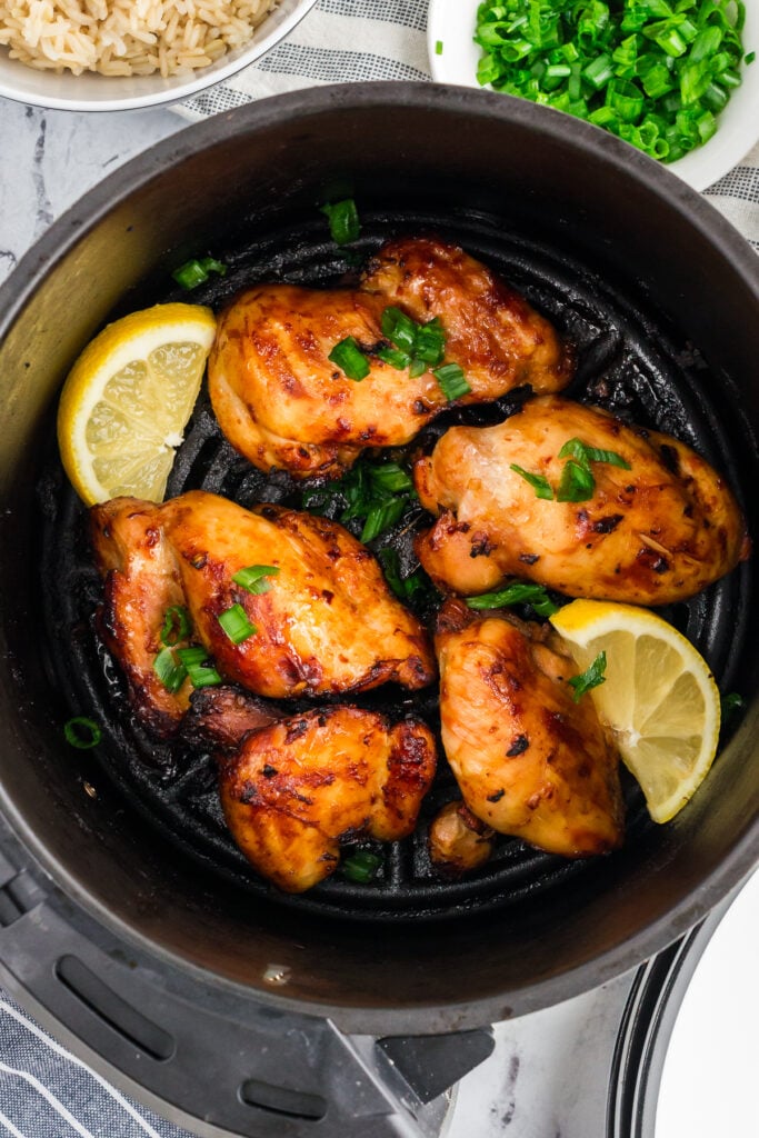 Boneless marinated chicken thighs in an air fryer basket, garnished with lemon and parsley. 