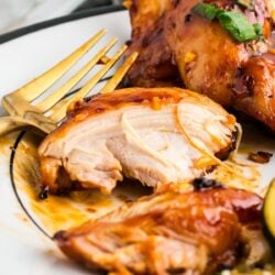 A piece of chicken thigh on a white plate with a gold fork.