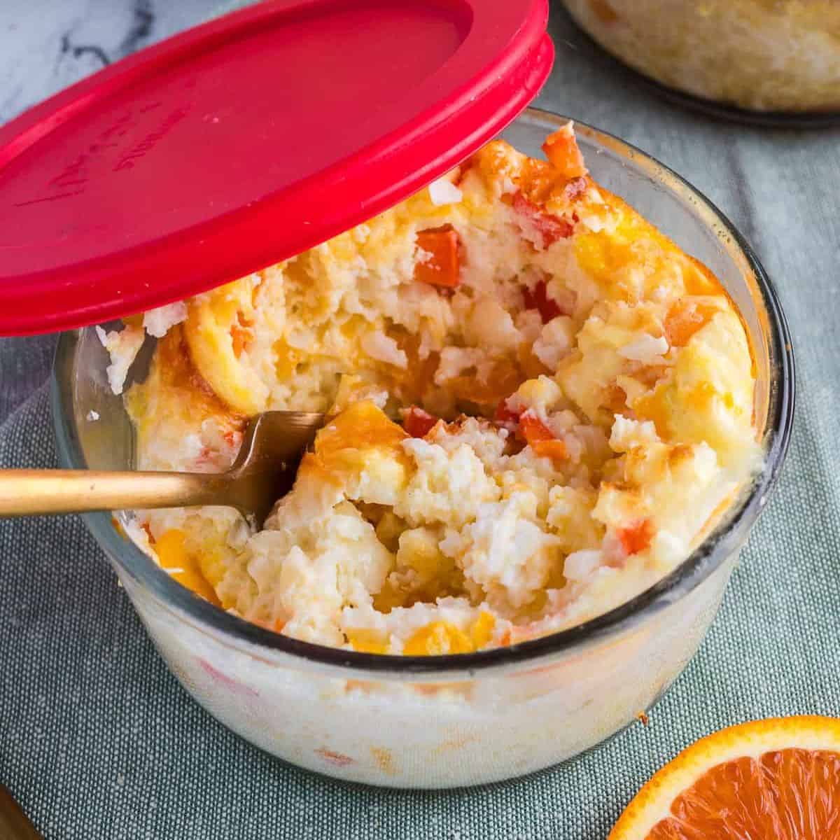 Breakfast meal prep bowls in a glass container with a red lid and a gold spoon inside.