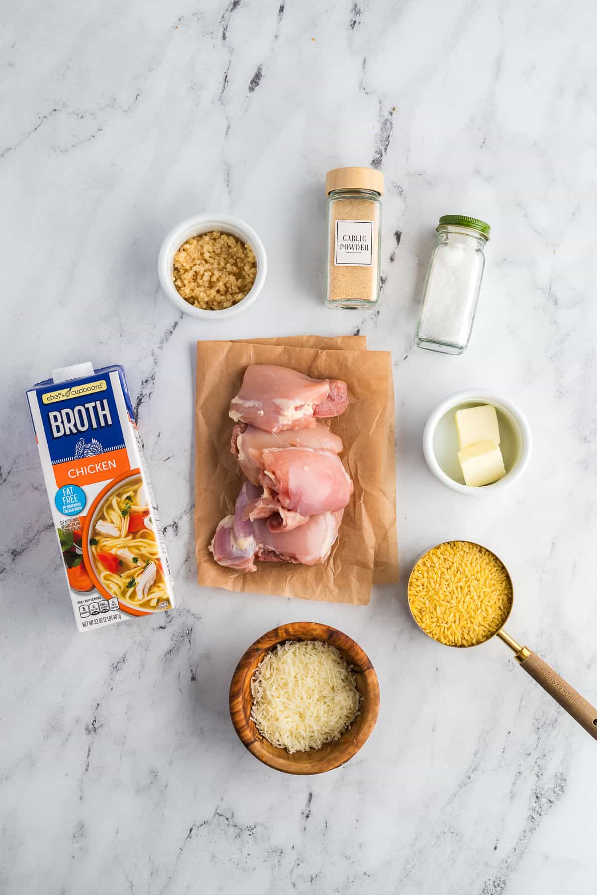 Ingredients for chicken and orzo skillet on a marble background in separate containers. 