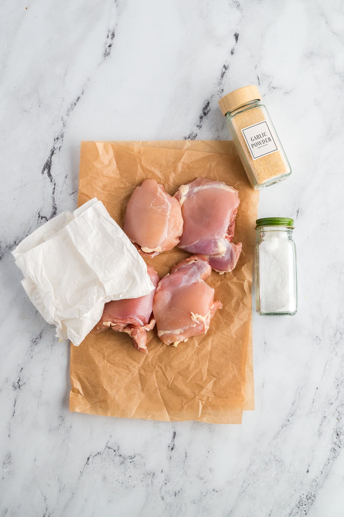 Chicken thighs on a piece of parchment before being seasoned with salt and garlic powder.