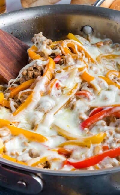 Chicken Cheesesteak Skillet in a metal skillet with a wooden spoon.