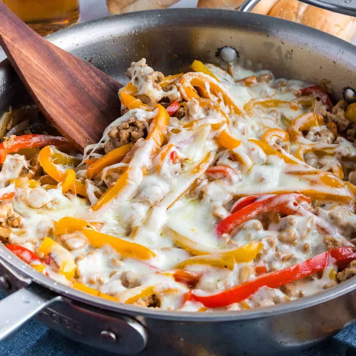 Chicken Cheesesteak Skillet in a metal skillet with a wooden spoon.
