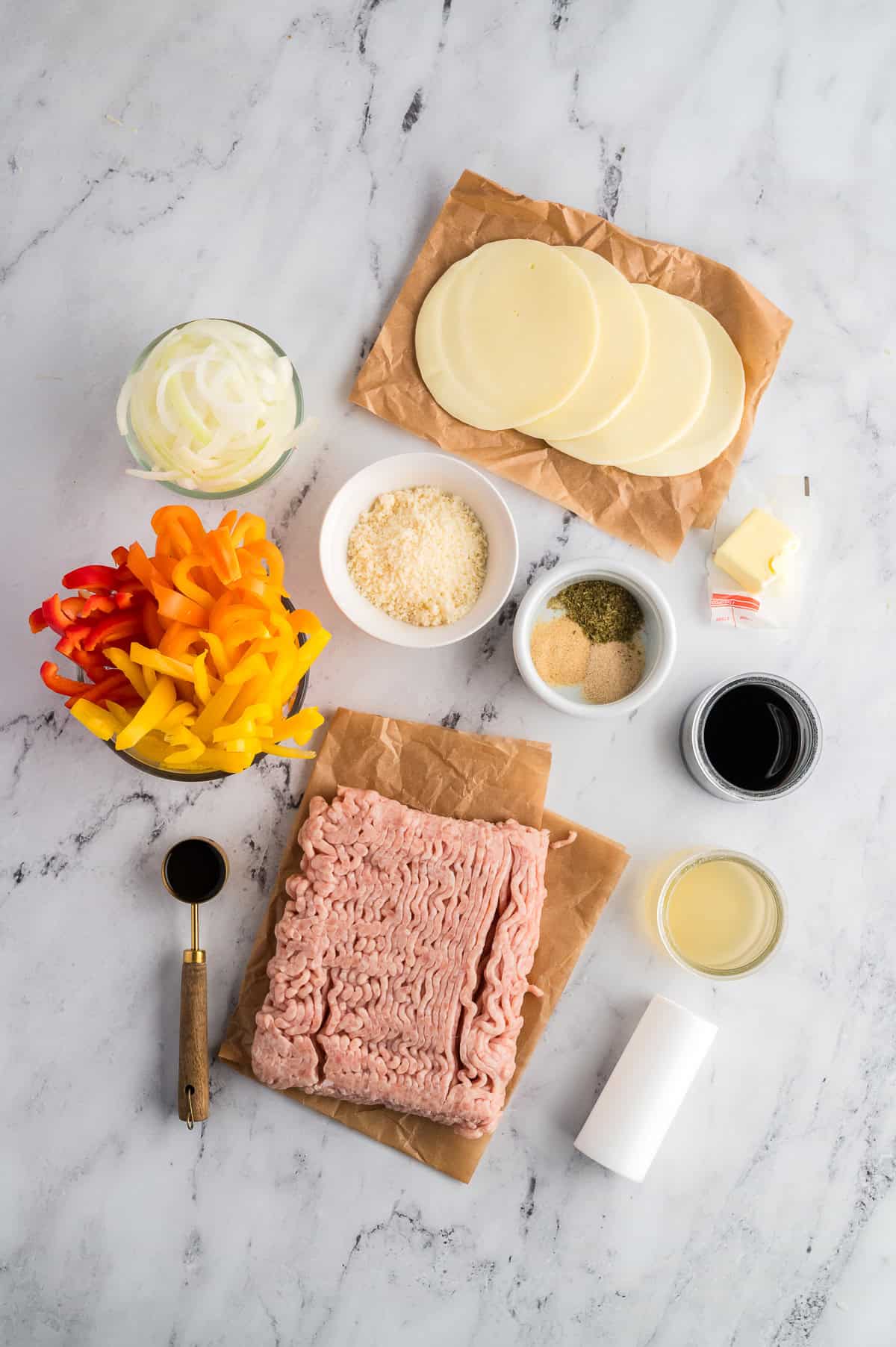 Ingredients for chicken cheesesteak casserole in separate containers on a marble background.