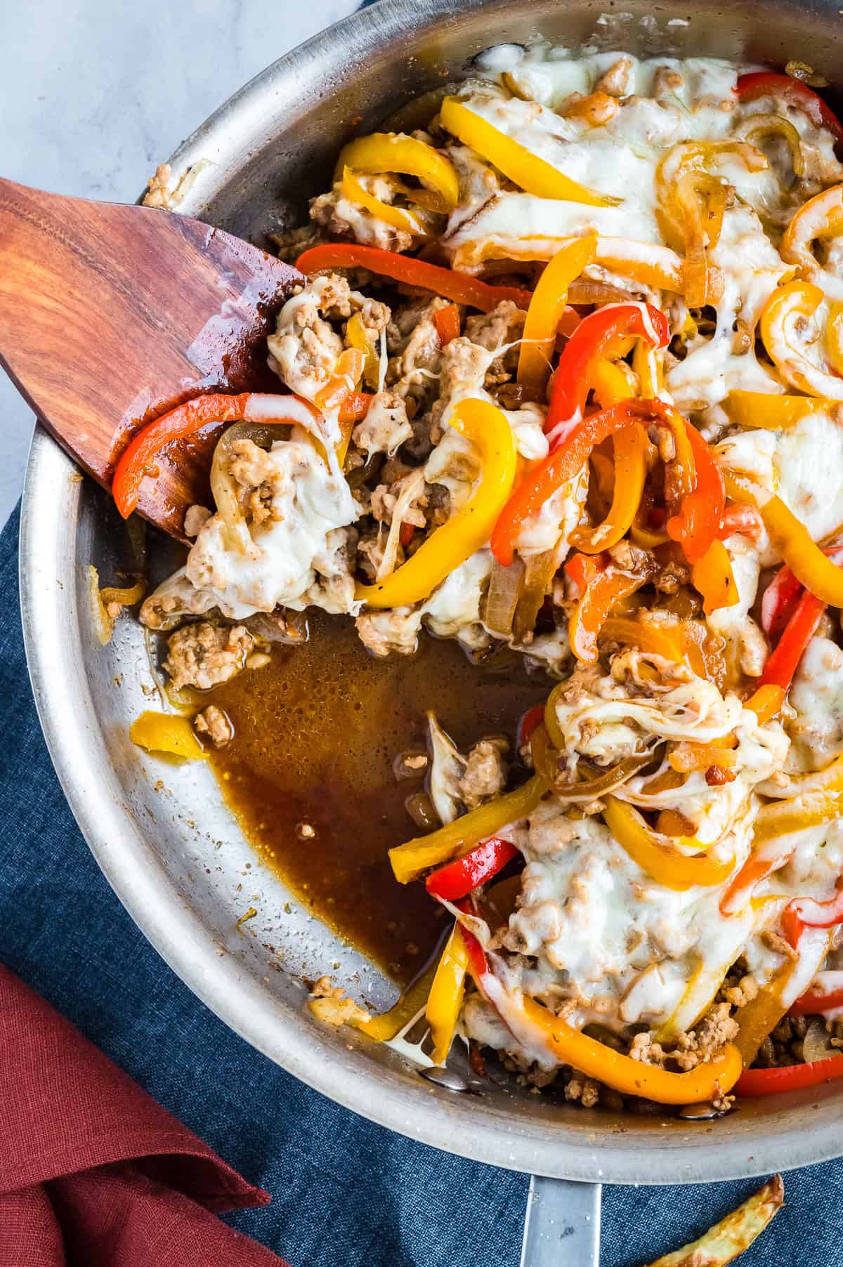 Finished chicken cheesesteak casserole in a skillet with a wooden spoon scooping some out.