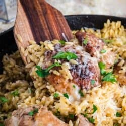 Chicken Orzo in a skillet with a wooden spoon inside.
