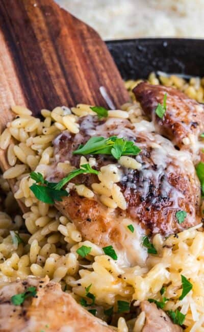 Chicken Orzo in a skillet with a wooden spoon inside.