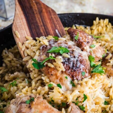 Chicken Orzo in a skillet with a wooden spoon inside.