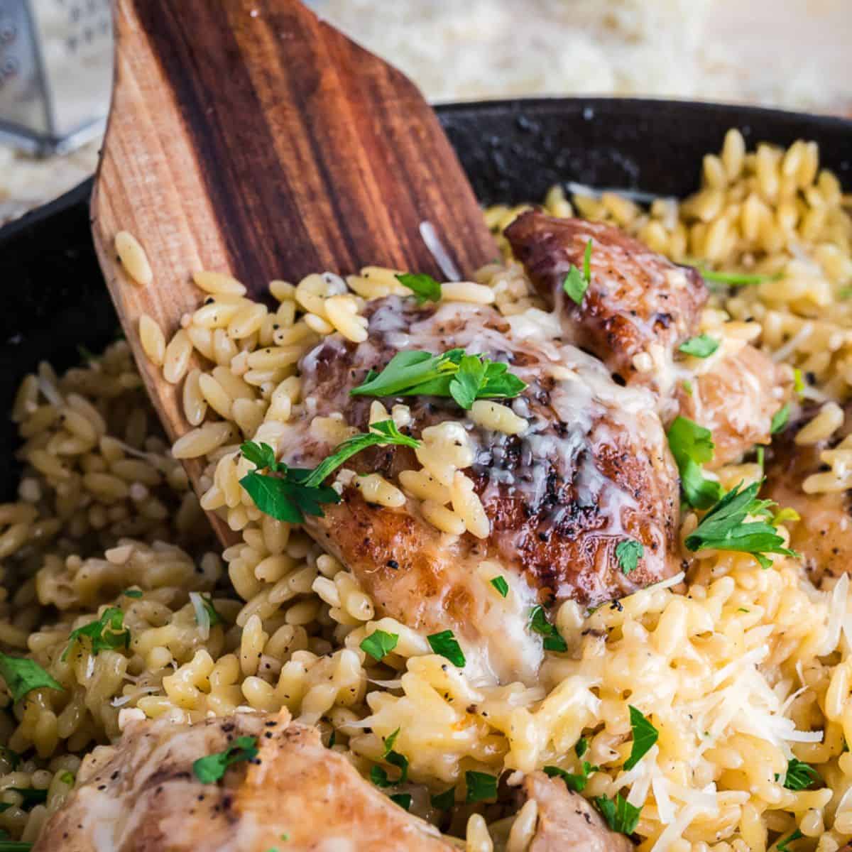 Chicken Orzo in a skillet with a wooden spoon inside.