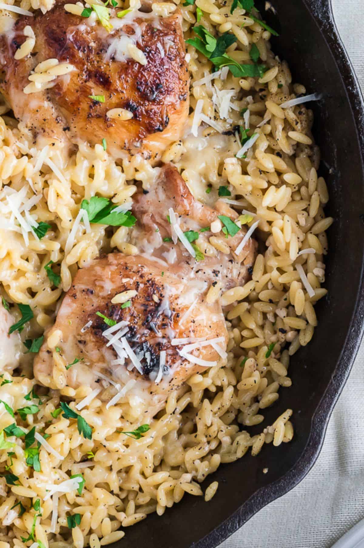 Cooked chicken and orzo in a skillet with parmesan and parsley on top.