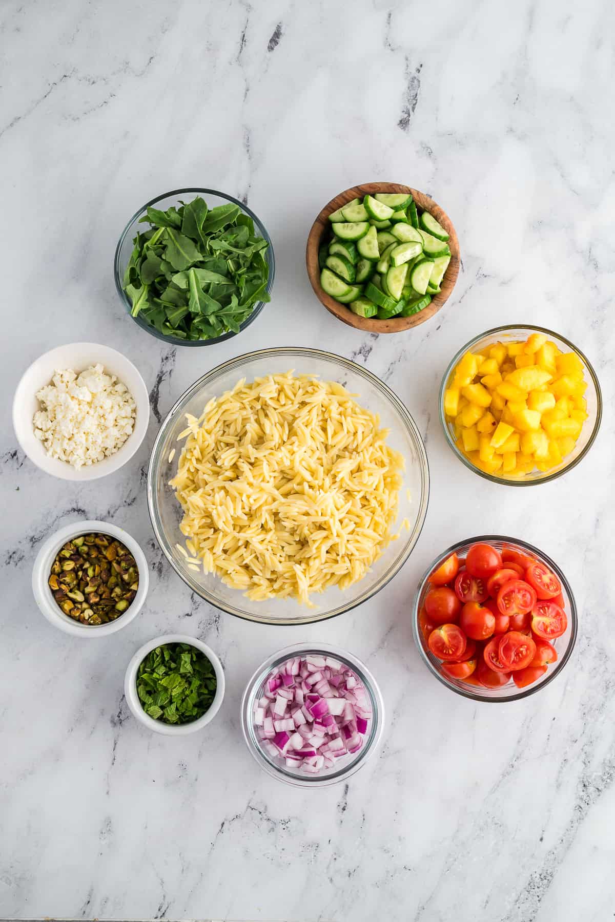 Ingredient for a peachy orzo salad arranged in clear bowls around the cooked orzo.
