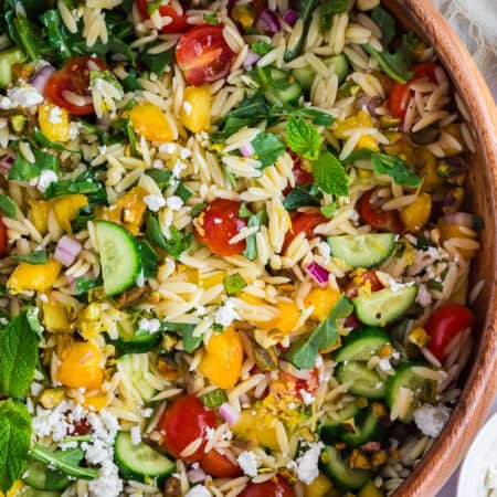 Close up of summer orzo salad with peaches, cherry tomatoes, cucumbers, and feta.